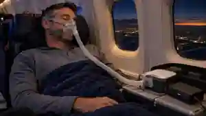 Пассажир спит с маской CPAP в самолёте; аппарат подключён к переносному аккумулятору